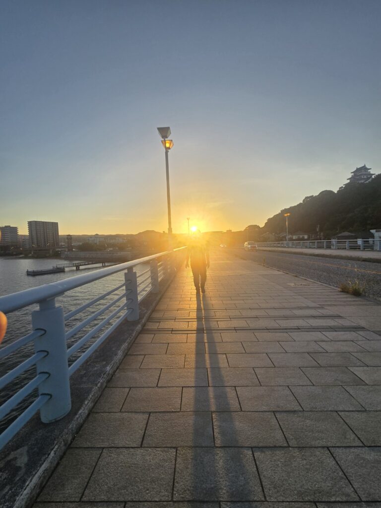 夏の夕暮れ、舞鶴橋から望む夕日と長い影が印象的な唐津の風景